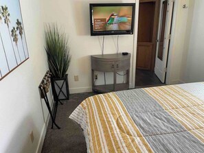 A bedroom with a bed, a television mounted on the wall, a plant, and a wooden cabinet.