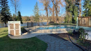 A backyard with a swimming pool, a wooden shed, and a stone pathway.