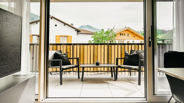 Uma varanda com mesa e cadeiras, um cercado de madeira e edifícios ao fundo.