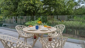 Una mesa redonda con cuatro sillas, un jarrón de flores y una planta pequeña en maceta en un balcón con barandilla de cristal.