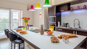 Ett modernt kök med en central köksö, rostfria vitvaror och färgglada hänglampor.