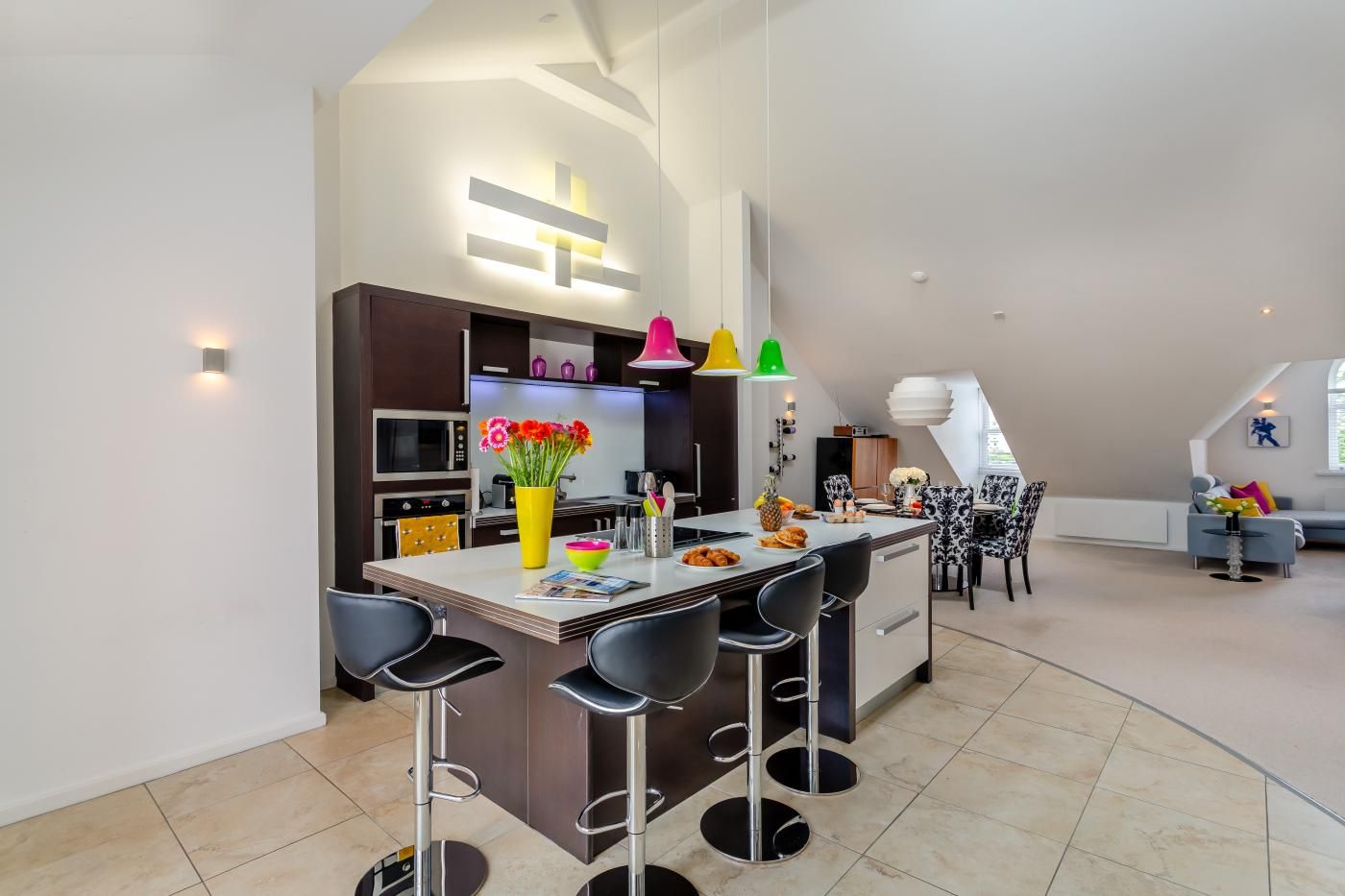 A modern kitchen with a central island, bar stools, and a dining area with a patterned chair.