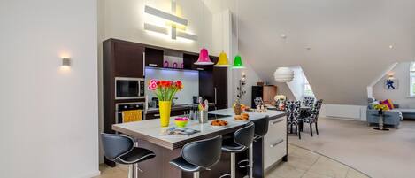 A modern kitchen with a central island, bar stools, and a dining area with a patterned chair.