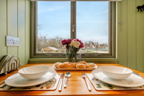 A dining table with two white bowls, a plate of rolls, and a vase with flowers.