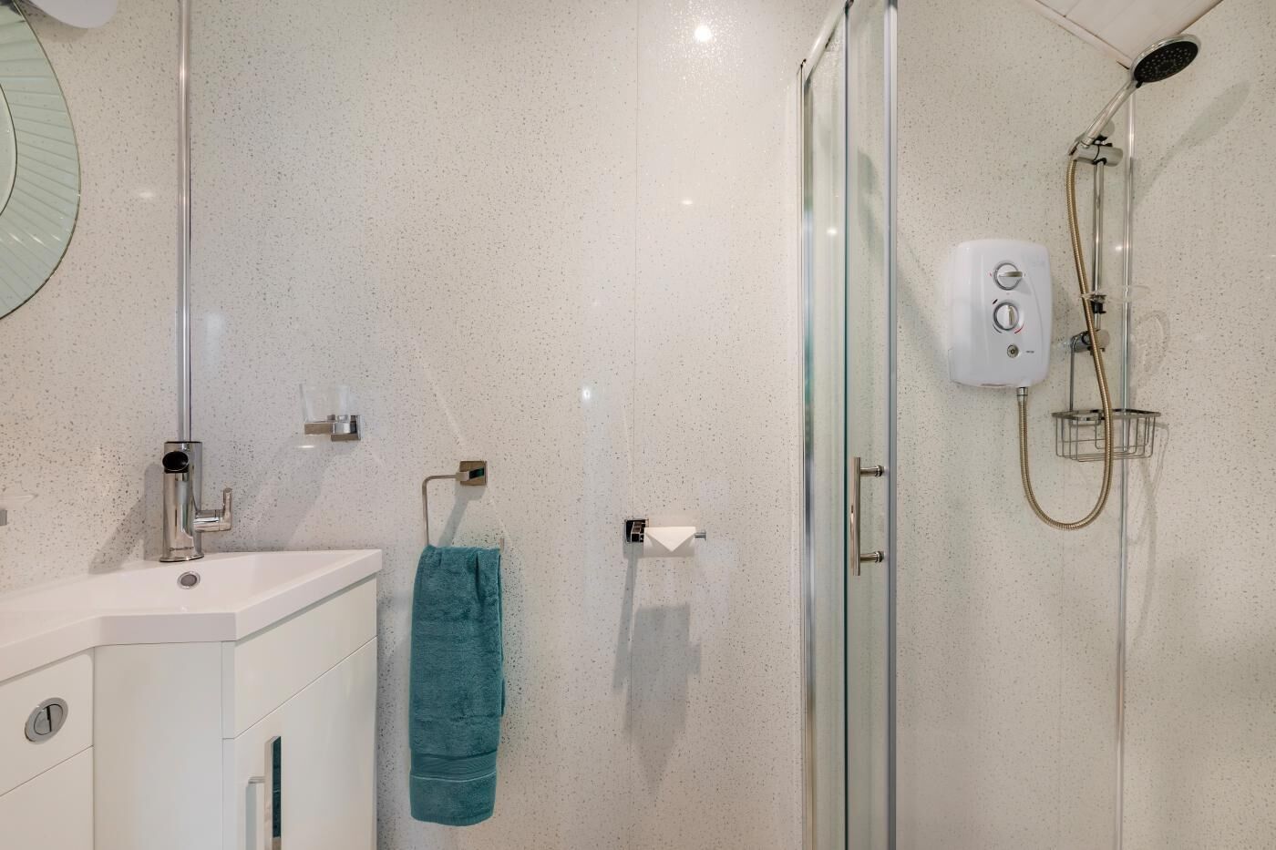 A modern bathroom with a glass shower enclosure, a white sink, and a towel rack.