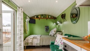 A room with a bed, a green sofa, a wooden table, a mirror, and a window with curtains. - 1 Bed in Marden (oc-c34994) (Horsmonden)