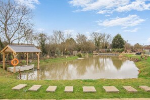 A pond with a wooden structure and a lifebuoy, surrounded by grass and trees.