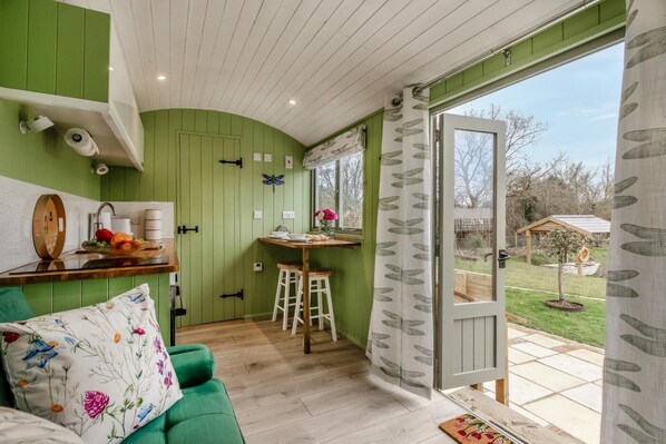 A room with a green wall, a wooden ceiling, a dining area with stools, a green sofa, and a view of the outdoors.