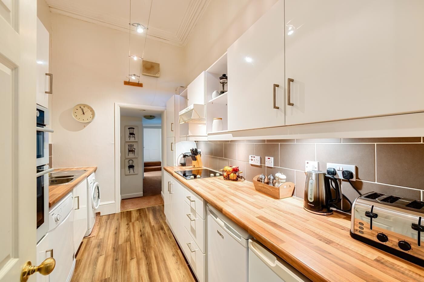 Una cocina moderna con armarios blancos, encimeras de madera, horno empotrado y cafetera.