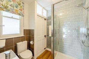 A bathroom with a toilet, sink, shower, and a window with a curtain. - 3 Bed in Ilfracombe (oc-h36896) (Ilfracombe)