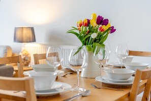 A dining table set with white plates, bowls, and wine glasses, with a vase of tulips in the center. - 3 Bed in Ilfracombe (oc-h36896) (Ilfracombe)