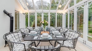 A conservatory with a glass roof, a dining table set for six, and chairs with checkered cushions. - 4 Bed in Beckley (oc-s34808) (Beckley)