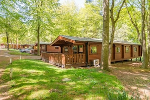 A row of wooden cabins with a deck, surrounded by trees in a campground. - 3 Bed in Kenwick (oc-l36924) (Legbourne)