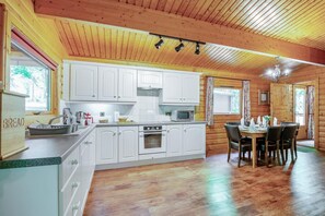 A wooden cabin interior with a kitchen and dining area, featuring white cabinetry, a stove, and a dining table with chairs. - 3 Bed in Kenwick (oc-l36924) (Legbourne)