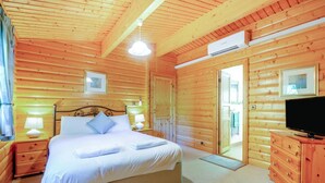 A wooden cabin bedroom with a bed, bedside lamps, a television, and a door leading outside. - 3 Bed in Kenwick (oc-l36924) (Legbourne)
