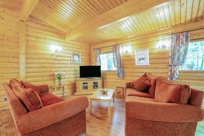 A log cabin interior with two sofas, a coffee table, a TV, and a window with curtains. - 3 Bed in Kenwick (oc-l36924) (Legbourne)