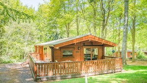 A wooden cabin with a porch, surrounded by trees. - 3 Bed in Kenwick (oc-l36924) (Legbourne)