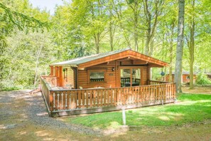 A wooden cabin with a porch, surrounded by trees. - 3 Bed in Kenwick (oc-l36924) (Legbourne)