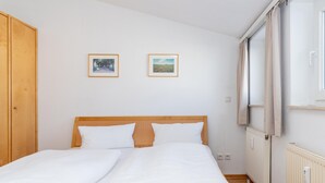 A bedroom with a wooden headboard, two beds, a window with curtains, and two framed pictures on the wall. - Attraktive Ferienwohnung fur Urlaub zu Zweit in Sellin (Sellin)