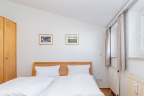 A bedroom with a wooden headboard, two beds, a window with curtains, and two framed pictures on the wall. - Attraktive Ferienwohnung fur Urlaub zu Zweit in Sellin (Sellin)