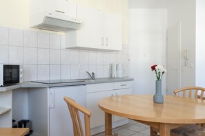 Une cuisine avec des meubles blancs, un four à micro-ondes, une machine à café et un vase rempli de fleurs posé sur la table.