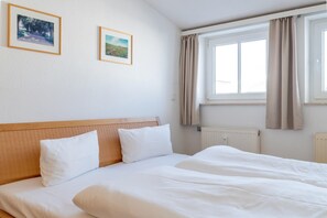 A hotel room with a large bed, two pillows, a headboard, a window with curtains, and two framed pictures on the wall. - Attraktive Ferienwohnung fur Urlaub zu Zweit in Sellin (Sellin)