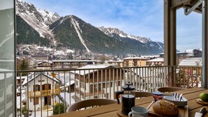 A balcony with a mountain view, a table with a coffee pot, cups, and a loaf of bread. - Central Chamonix Apartment With Views (Chamonix-Mont-Blanc)