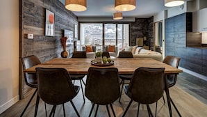 A modern dining room with a wooden table, black chairs, and pendant lights. - Central Chamonix Apartment With Views (Chamonix-Mont-Blanc)