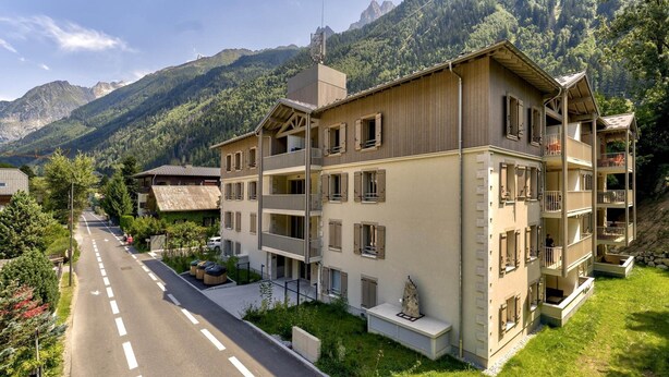 A multi-story hotel with balconies, a parking area, and a mountain backdrop. - Central Chamonix Apartment With Views (Chamonix-Mont-Blanc)