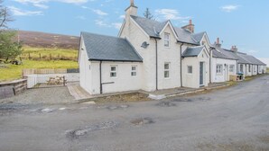 A row of white buildings with grey roofs, a gravel driveway, and a grassy field in the background. - 3 Bed in Wanlockhead (oc-g36354) (Wanlockhead)