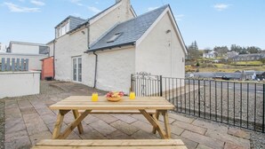 A white house with a tiled roof, a wooden table with a bowl of fruit and drinks, and a metal fence. - 3 Bed in Wanlockhead (oc-g36354) (Wanlockhead)