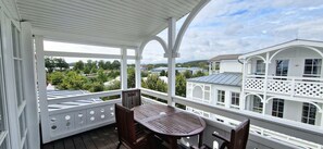 Ein überdachter Balkon mit Tisch und Stühlen, mit Blick auf ein Wohngebiet mit Häusern und Grünflächen.