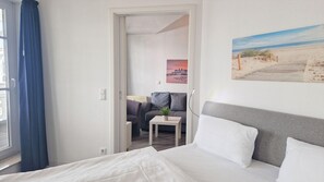 A hotel room with a bed, a small table with a plant, a sofa, and a painting of a beach scene. - Geschmackvoll Eingerichtete Ferienwohnung mit Balkon in Sellin (Sellin)