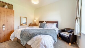Een slaapkamer met een bed, nachtkastje, lamp, kledingkast en een stoel.