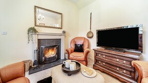 Een woonkamer met een open haard, een leren fauteuil, een televisie en een houten kast.