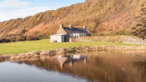 Een huis met een stenen schoorsteen, een klein terras en een vijver ervoor.