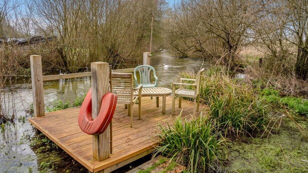 Un muelle de madera con sillas y un flotador salvavidas, rodeado de agua y vegetación.