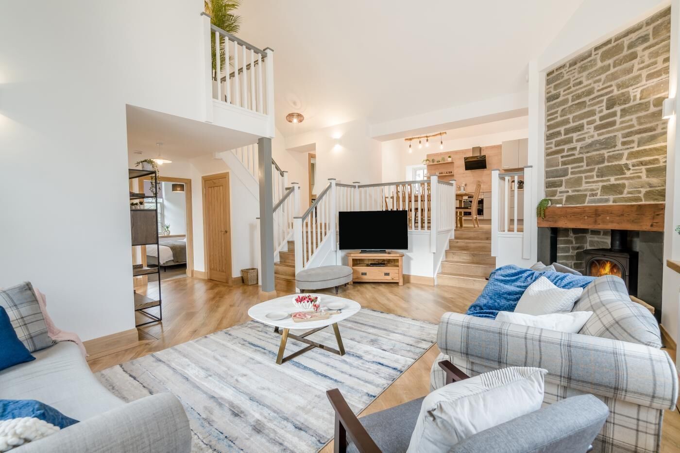 A spacious living room with a fireplace, a staircase leading to a loft, and a kitchen in the background.