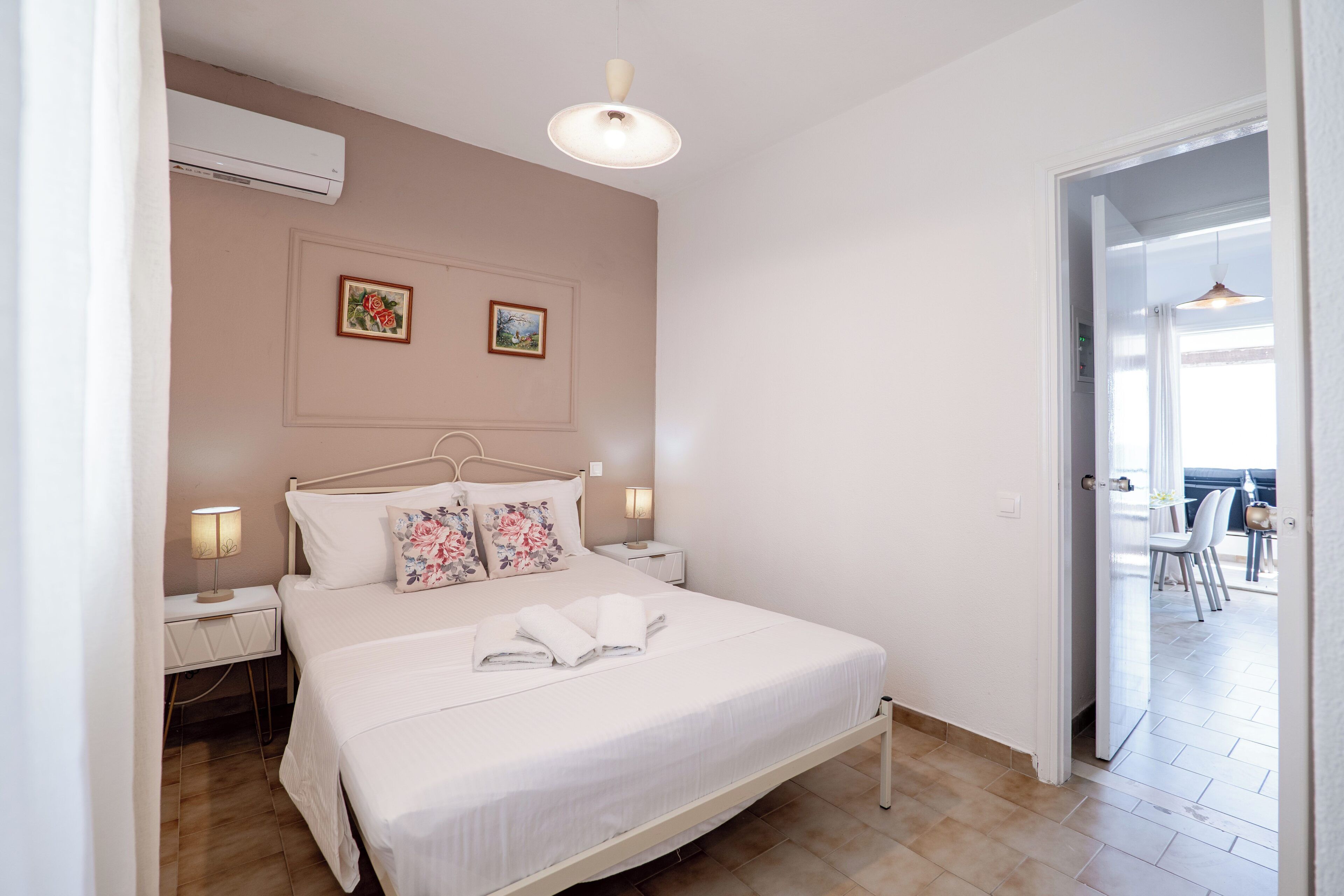 Quarto com cama, mesas de cabeceira, ar condicionado fixado na parede e uma porta que dá para uma varanda.