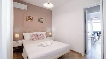 Quarto com cama, mesas de cabeceira, ar condicionado fixado na parede e uma porta que dá para uma varanda.