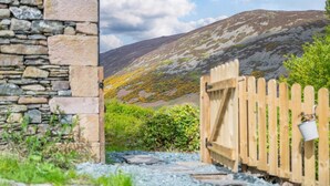 A stone building with a wooden gate, a stone wall, and a mountain in the background. - 1 Bed in Mosedale (oc-b37510) (Mosedale)