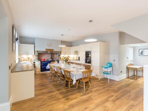 Een moderne keuken met houten vloeren, een eethoek met een tafel gedekt voor vier personen, en een klein zithoekje met een kinderstoel.