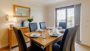 A dining area with a wooden table, black chairs, a mirror, and a view of the sea. - 4 Bed in Redruth (oc-06457) (Portreath)