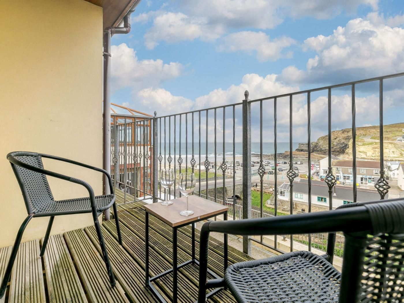 A balcony with two chairs, a table, and a view of the sea and town.