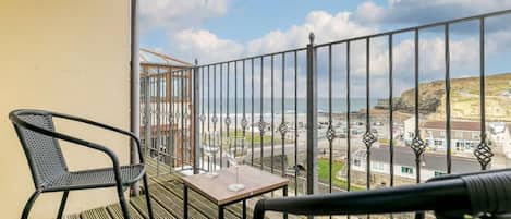 A balcony with two chairs, a table, and a view of the sea and town.