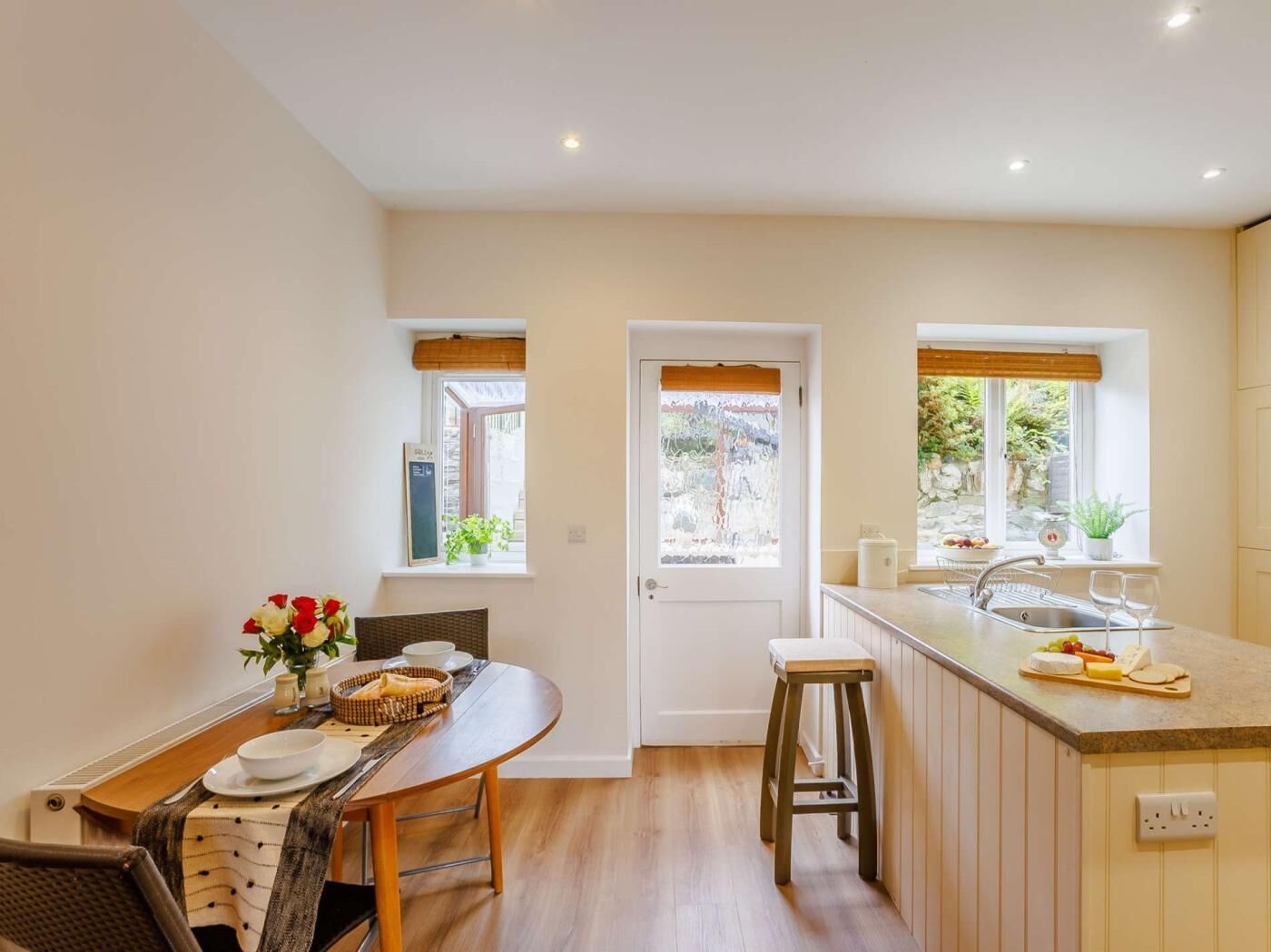 A modern kitchen with a dining area, wooden flooring, and windows with views.