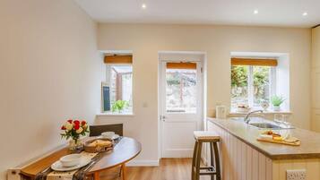 A modern kitchen with a dining area, wooden flooring, and windows with views.
