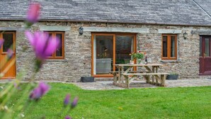 A stone building with a wooden table and chairs in front, large windows, and a grassy yard. - 2 Bed in St. Ervan (oc-s36909) (Saint Ervan)