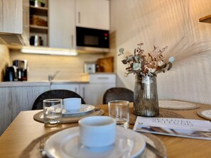 Une table à manger ornée d’un vase de fleurs séchées, d’un magazine et d’une tasse.