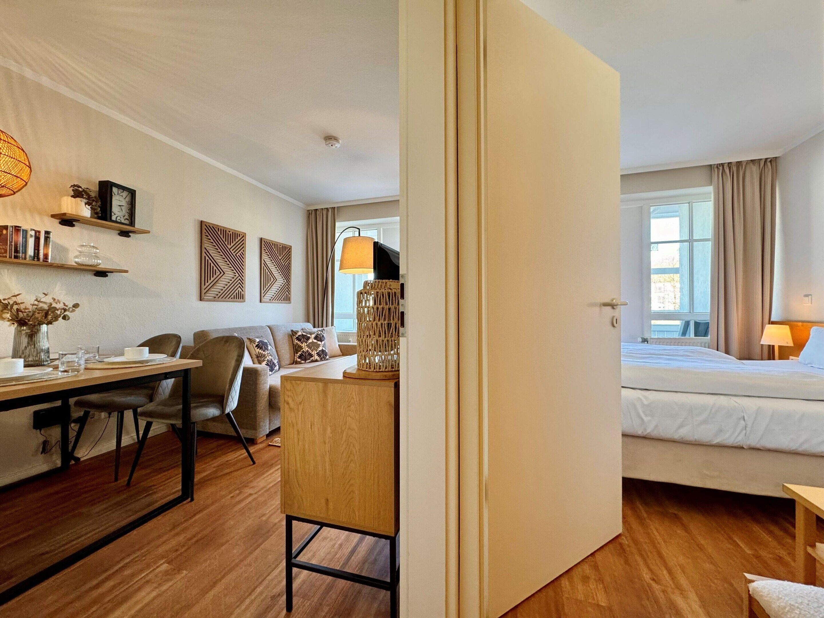 A hotel room with a bed, a desk with a chair, a sofa, a lamp, and a window with curtains.